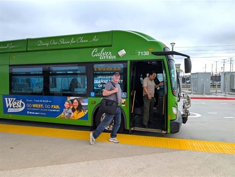 En man med väska kliver av en grön Culver City-buss vid en hållplats.